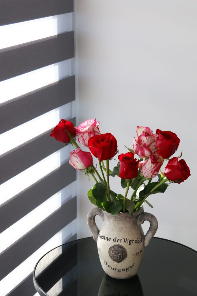 A stunning bouquet of red and white roses in a vintage ceramic vase on a round black table.