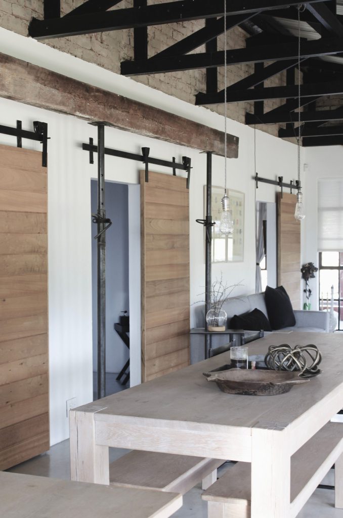 Contemporary indoor space featuring rustic barn doors and a minimalist table with hanging lights.