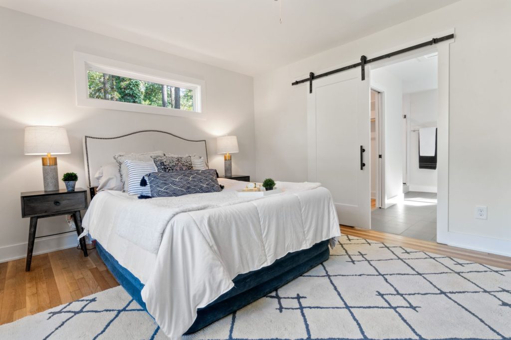 A bright, modern bedroom featuring a neatly arranged bed, wooden flooring, and decorative elements.